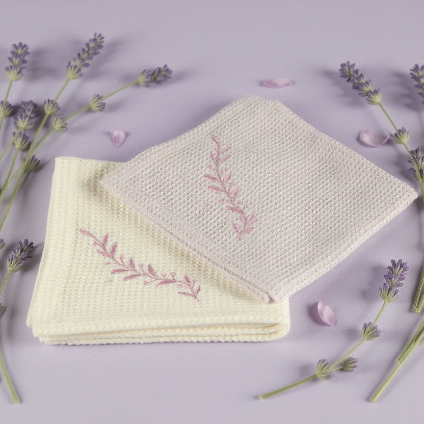 Folded fabric with embroidered design surrounded by lavender flowers on a light purple background