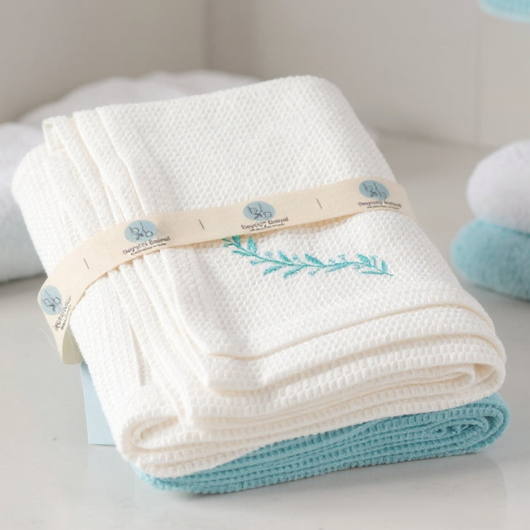 Folded white towel with blue accents and a brand logo on a light surface.