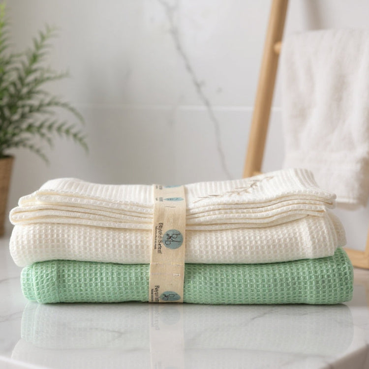 Stack of folded towels on a marble surface with a plant and towel rack in the background