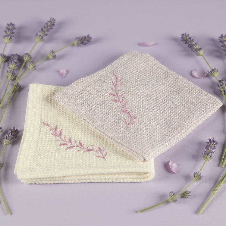 Folded fabric with embroidered design surrounded by lavender flowers on a light purple background