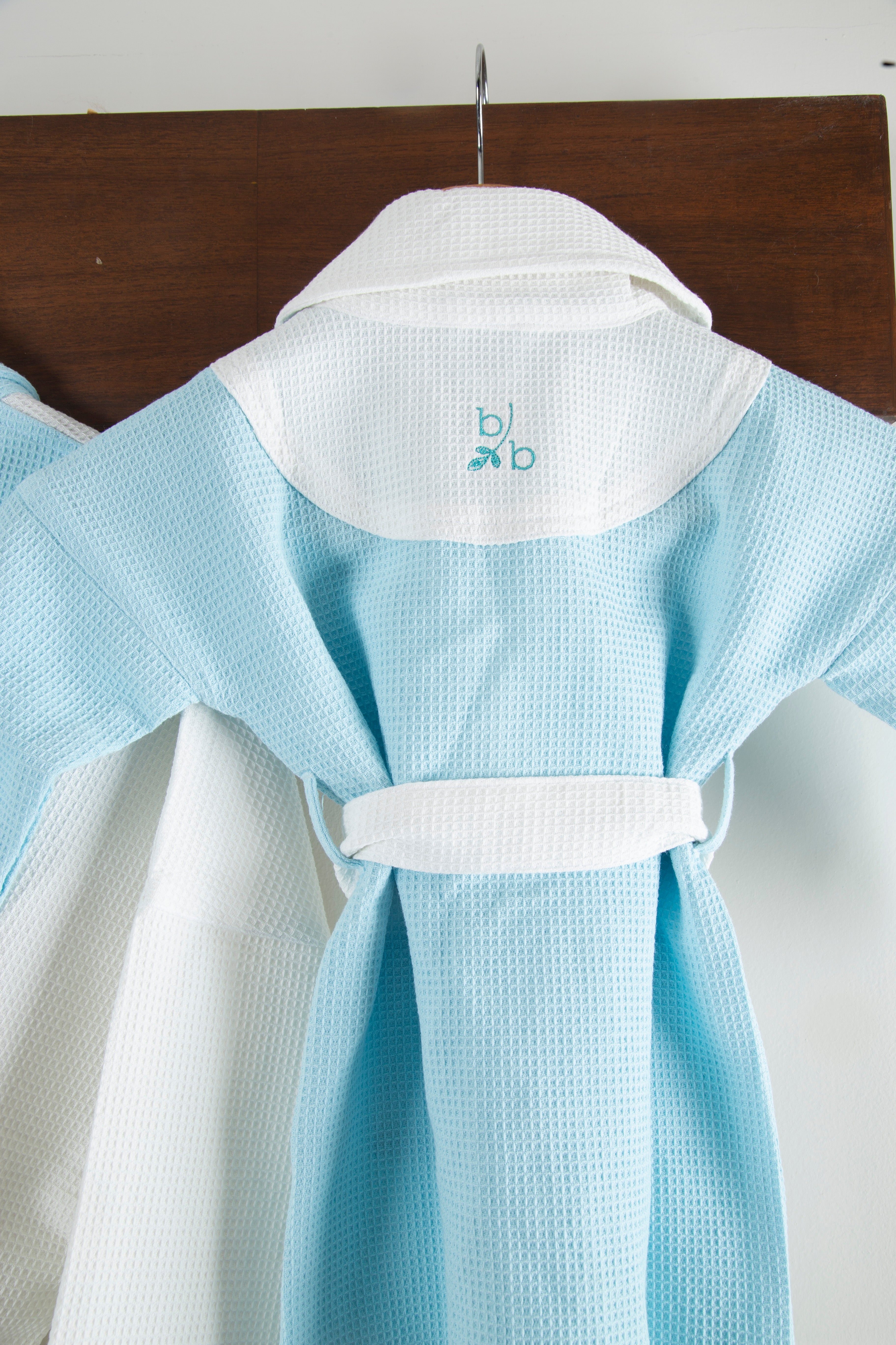 Light blue and white kids bathrobes garment with a brand logo on a wooden surface